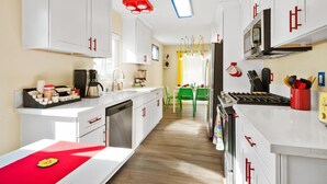 A modern kitchen with white cabinets, a dishwasher, a stove, and a dining area with green chairs. - LEGO Dream! 🧱🌊🕹️⛳🎥 Heated Pool, Theater, Arcade, & more! (Garden Grove)
