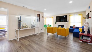A modern living room with a fireplace, a TV, and a play area with toys and a toy car. - LEGO Dream! 🧱🌊🕹️⛳🎥 Heated Pool, Theater, Arcade, & more! (Garden Grove)