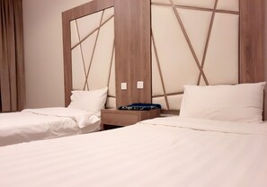 Una cama doble con ropa de cama blanca, una mesita de noche de madera con un objeto de diseño azul y blanco encima, y un cabecero con diseño geométrico.