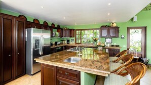 Une cuisine spacieuse dotée d’un grand îlot central, de meubles en bois foncé, d’appareils électroménagers en acier inoxydable et d’un mur d’accent vert.