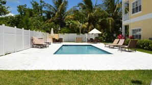A rectangular swimming pool with lounge chairs and umbrellas, surrounded by a white fence and palm trees. - Luxury Condo at Venito (Nassau)
