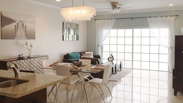 A modern dining area with a chandelier, a ceiling fan, and a large window with curtains. - Luxury Condo at Venito (Nassau)