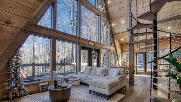 A spacious loft-style room with a large window, a cozy sectional sofa, a fireplace, and a spiral staircase. - Once Upon A Time is a beautiful A-Frame Cabin thats magical with a unique style (Gatlinburg)