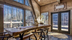 A wooden interior with a long table and chairs, large windows, and a view of trees. - Once Upon A Time is a beautiful A-Frame Cabin thats magical with a unique style (Gatlinburg)