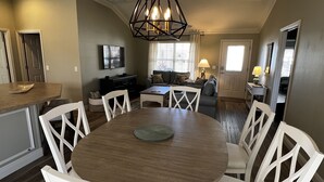 Un coin repas avec une table ronde, des chaises blanches, un plafond en bois et un luminaire suspendu noir.