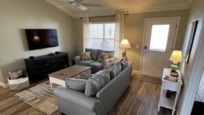 Un salon avec un canapé gris, une table basse, un téléviseur et un ventilateur de plafond.