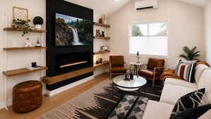 Una sala de estar con chimenea, televisión, asientos cómodos y un ventanal grande.