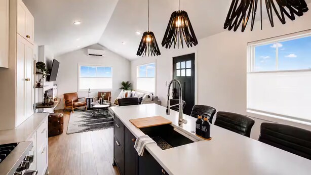 Una cocina moderna con una isla central, iluminación colgante y vistas al área de estar.