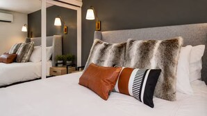 Una habitación de hotel moderna con una cama grande, varios almohadones, un cabecero y lámparas fijadas a la pared.
