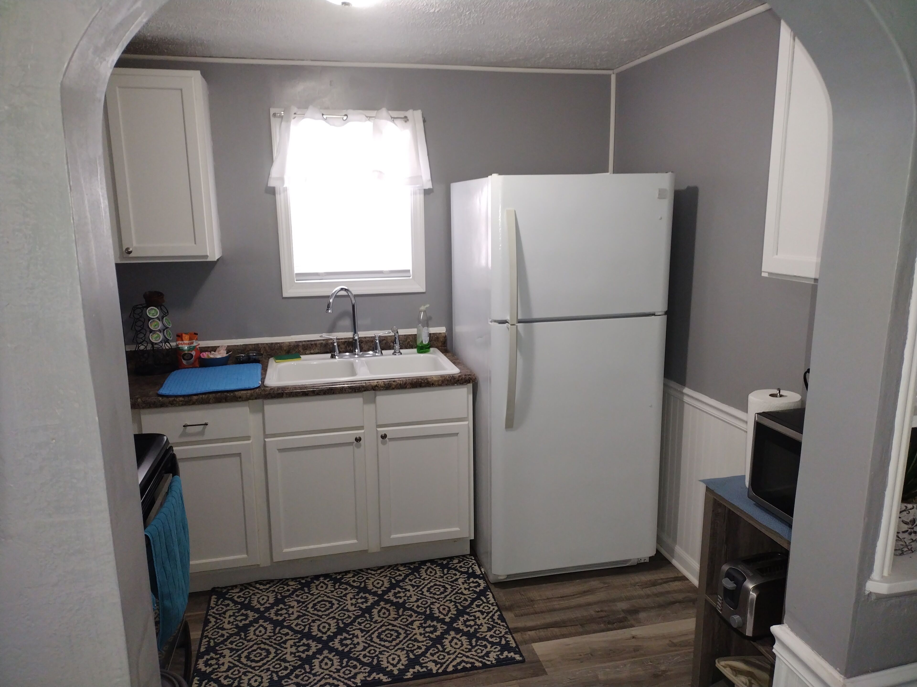 A compact kitchen with white cabinets, a double sink, a refrigerator, and a microwave.