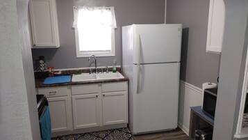 A compact kitchen with white cabinets, a double sink, a refrigerator, and a microwave.