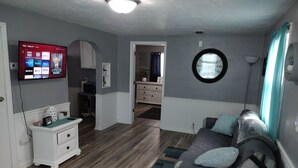 Ein Wohnzimmer mit Fernseher, der Streaming-Dienste anzeigt, einer Couch, einem Couchtisch und einem runden Fenster.