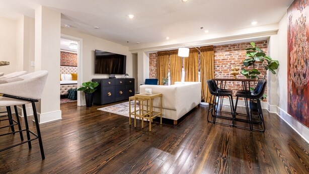 Una sala de estar moderna con pared de ladrillo, un sofá blanco, una mesa de centro de madera y una zona de bar con taburetes.