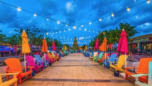 Un espace extérieur aménagé avec des chaises Adirondack colorées et des parasols, le tout illuminé par des guirlandes lumineuses.