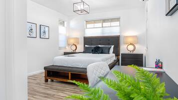 A modern bedroom with a bed, bedside tables, and a desk with a plant.