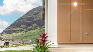 A modern building with a wooden door, a driveway, and a mountain in the background. - 🌺 Oahu Ocean & Mountain Views • Sleeps 14 • Pool, Spa, Near Beach, AC & BBQ 🌺 (Waianae)
