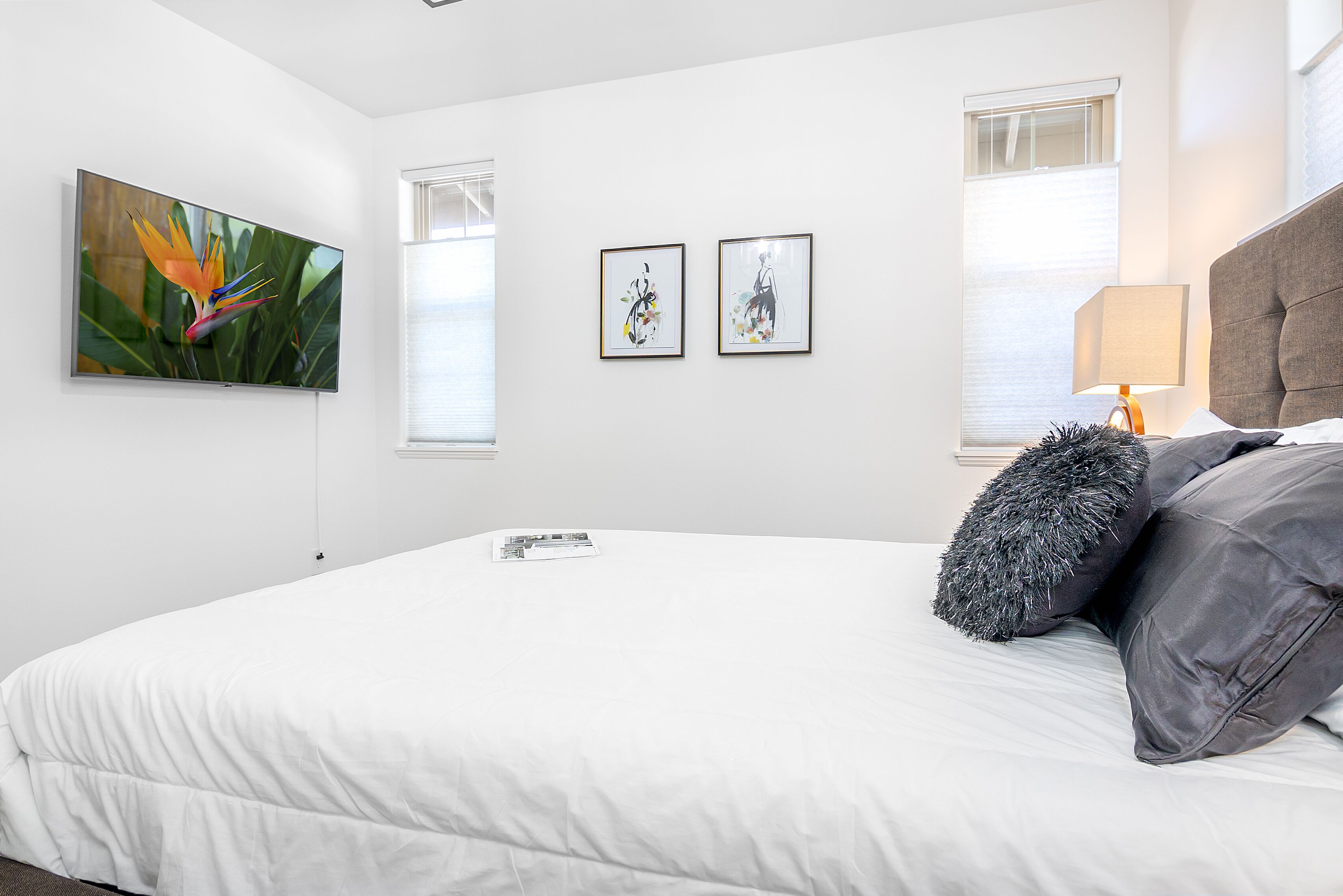Ein modernes Schlafzimmer mit einem großen Bett, einem flachbildfernseher an der Wand und zwei gerahmten Kunstwerken darüber.