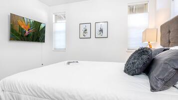 Ein modernes Schlafzimmer mit einem großen Bett, einem flachbildfernseher an der Wand und zwei gerahmten Kunstwerken darüber.