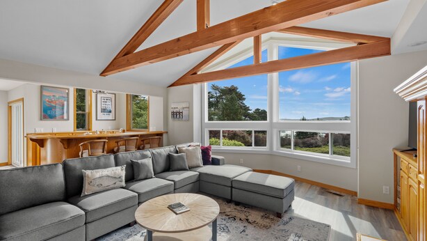 A spacious living room with a large sectional sofa, a coffee table, and a kitchen area with wooden cabinets and a dining table. - Renovated home w/ breathtaking views of the bay and new hot tub (Bodega Bay)