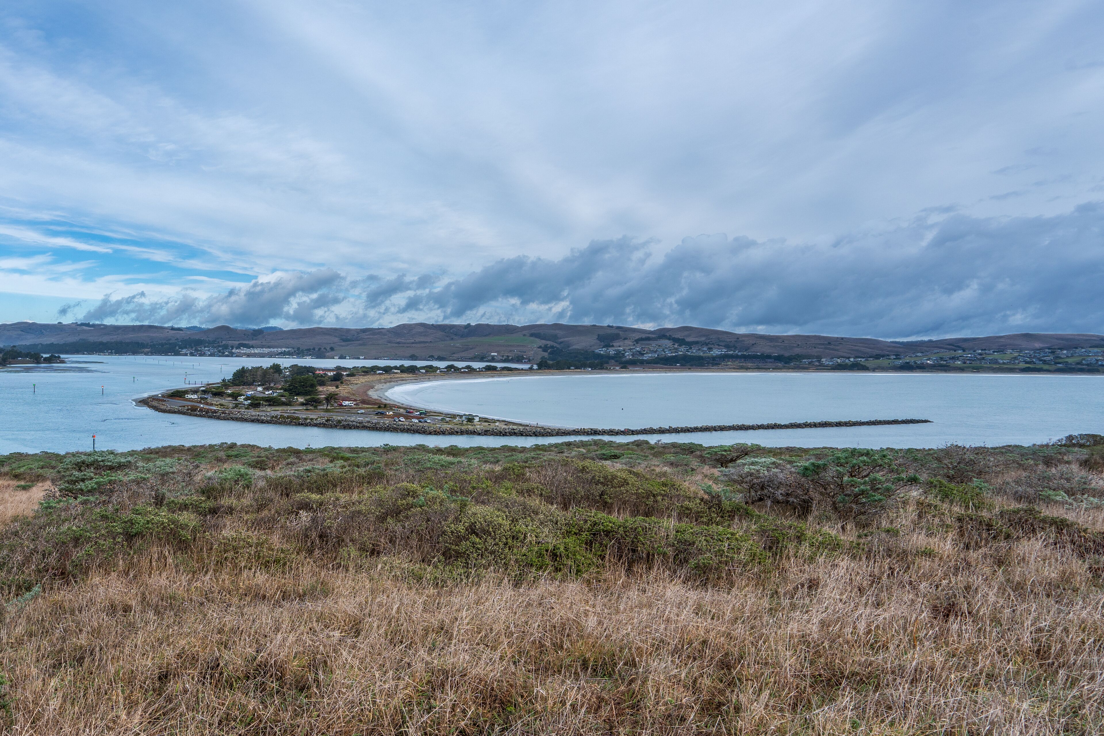Een kustlandschap met een golvende kustlijn, een klein eiland met gebouwen, en een stad in de verte.