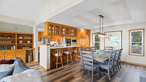 A spacious kitchen with wooden cabinets, a central island, and a dining area with a large table and chairs. - Renovated home w/ breathtaking views of the bay and new hot tub (Bodega Bay)