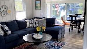 A modern living room with a dark blue sofa, a round coffee table with a decorative bowl, and a colorful rug. - Lazy Days: mid-term private waterfront cottage at the lake (Brighton)