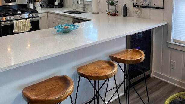 A modern kitchen with a large island, bar stools, pendant lighting, and a coffee mug rack. - Lazy Days: mid-term private waterfront cottage at the lake (Brighton)