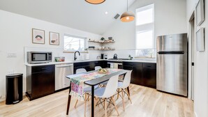 A modern kitchen with a dining table, chairs, a refrigerator, and a microwave.