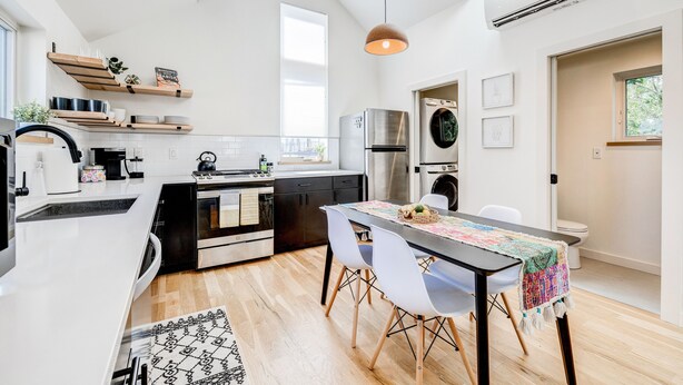 A modern kitchen with white cabinetry, a stainless steel refrigerator, and a dining area with a table and chairs.