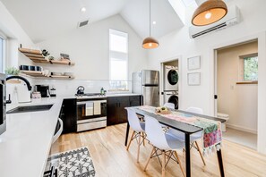 A modern kitchen with white cabinetry, a stainless steel refrigerator, and a dining area with a table and chairs. - Stylish 2BR Guesthouse w/ Private Patio - Walk to Tennyson St (Denver)