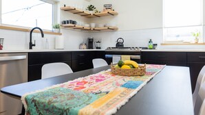 A modern kitchen with a dining table, a coffee machine, and a fruit basket.