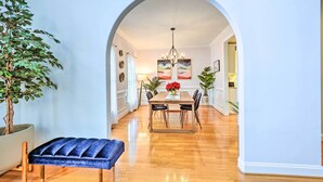 A dining area with a wooden table, chairs, and a chandelier. There is a potted plant and a bench in the foreground. - Tranquil Greensboro Home w/ Fire Pit! (Greensboro)