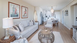 Un salon moderne avec un canapé gris, une table basse ronde en osier et un coin repas comprenant une table et des chaises blanches.