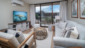 Un salon moderne doté d’un grand téléviseur à écran plat, d’un canapé, d’une table basse et d’un balcon offrant une vue sur les immeubles.