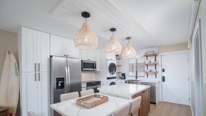 Une cuisine moderne avec des meubles blancs, des appareils en acier inoxydable, un îlot central et des suspensions en osier.