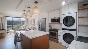 Une cuisine moderne dotée d’un îlot central, d’appareils électroménagers en acier inoxydable et de luminaires suspendus.