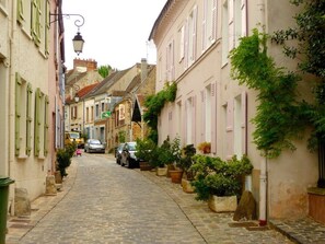 A narrow cobblestone street lined with historic buildings, some with shutters and potted plants. - Apartment Village de L'Escale de Neauphle (Neauphle-le-Château)