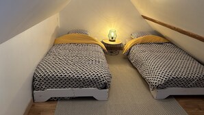A small, triangular attic bedroom with two beds, a nightstand, and a lamp.