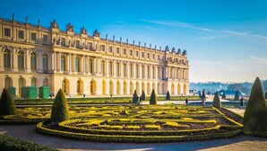 A grand palace with a symmetrical garden featuring geometric patterns and topiary.
