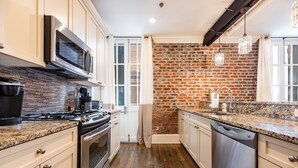 Een moderne keuken met een bakstenen muur, roestvrijstalen apparatuur en een granieten aanrecht.