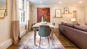 Een eetgedeelte met een houten tafel, stoelen, een bank en een kleurrijk vloerkleed.