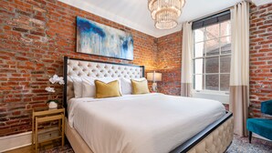 Een slaapkamer met een bakstenen muur, een groot bed, een kroonluchter en een raam met gordijnen.