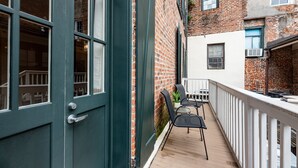 Een houten terras met een witte balustrade, een deur met raam, en een bakstenen muur.