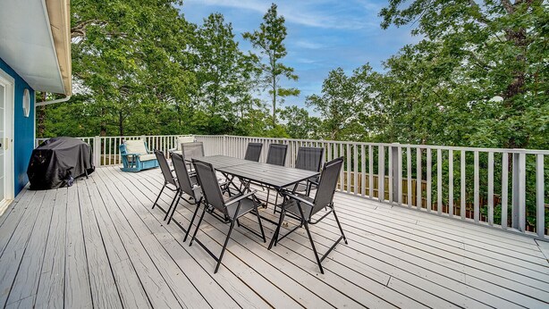 Une terrasse extérieure couverte, dotée d’une table et de chaises, entourée d’une balustrade blanche et d’arbres.