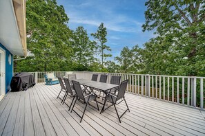 A covered outdoor deck with a table and chairs, surrounded by a white railing and trees.