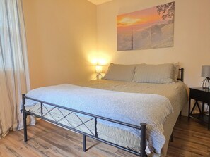 Een netjes opgemaakt bed met een hoofdeinde, een bedlampje en een aan de muur hangend schilderij.