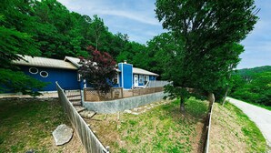 A house with a blue exterior, a fenced yard, and a tree in front.