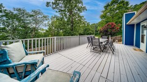A wooden deck with outdoor furniture, a railing, and a view of trees and a building.