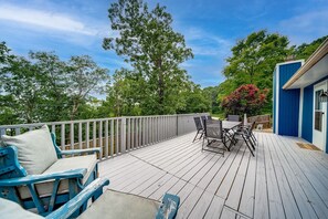 A wooden deck with outdoor furniture, a railing, and a view of trees and a building.