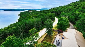 A coastal road winding through dense greenery, leading to a house with a visible deck and outdoor seating area.